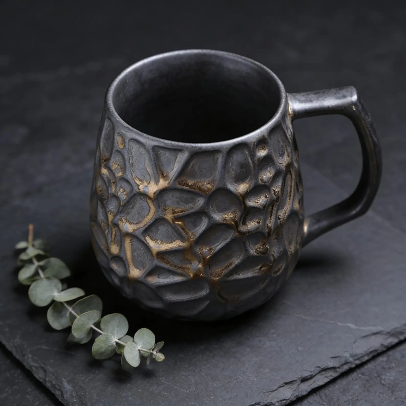 Carved dark mug with gold texture detail and eucalyptus